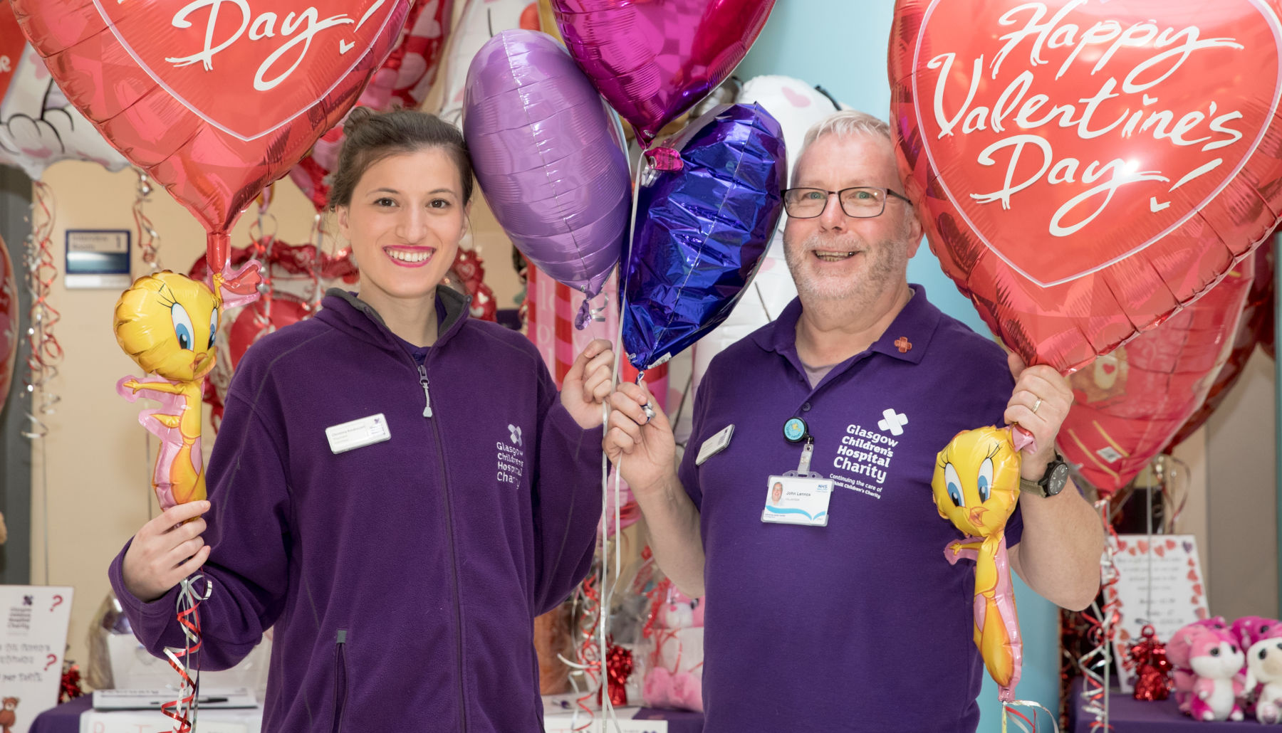 Two volunteers standing smiling at the camera holding large Valentines Day balloons