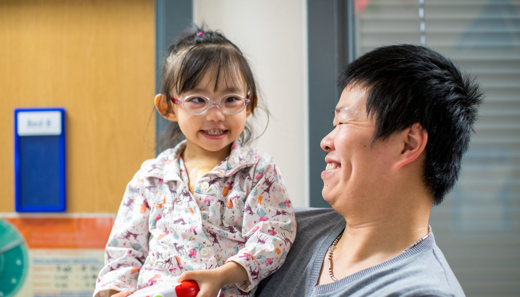 Father holding daughter in his arms while they smile at each other on the ward.