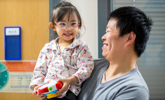 Father holding daughter in his arms while they smile at each other on the ward. 