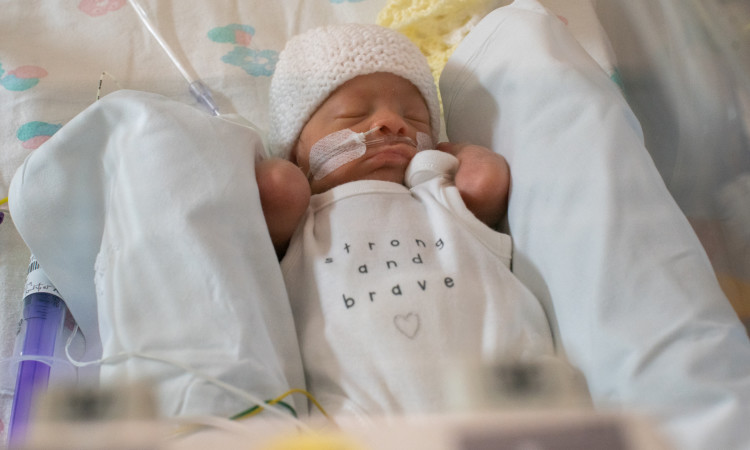 Baby Jaxon lies in his incubator in a white vest which reads Strong and Brave
