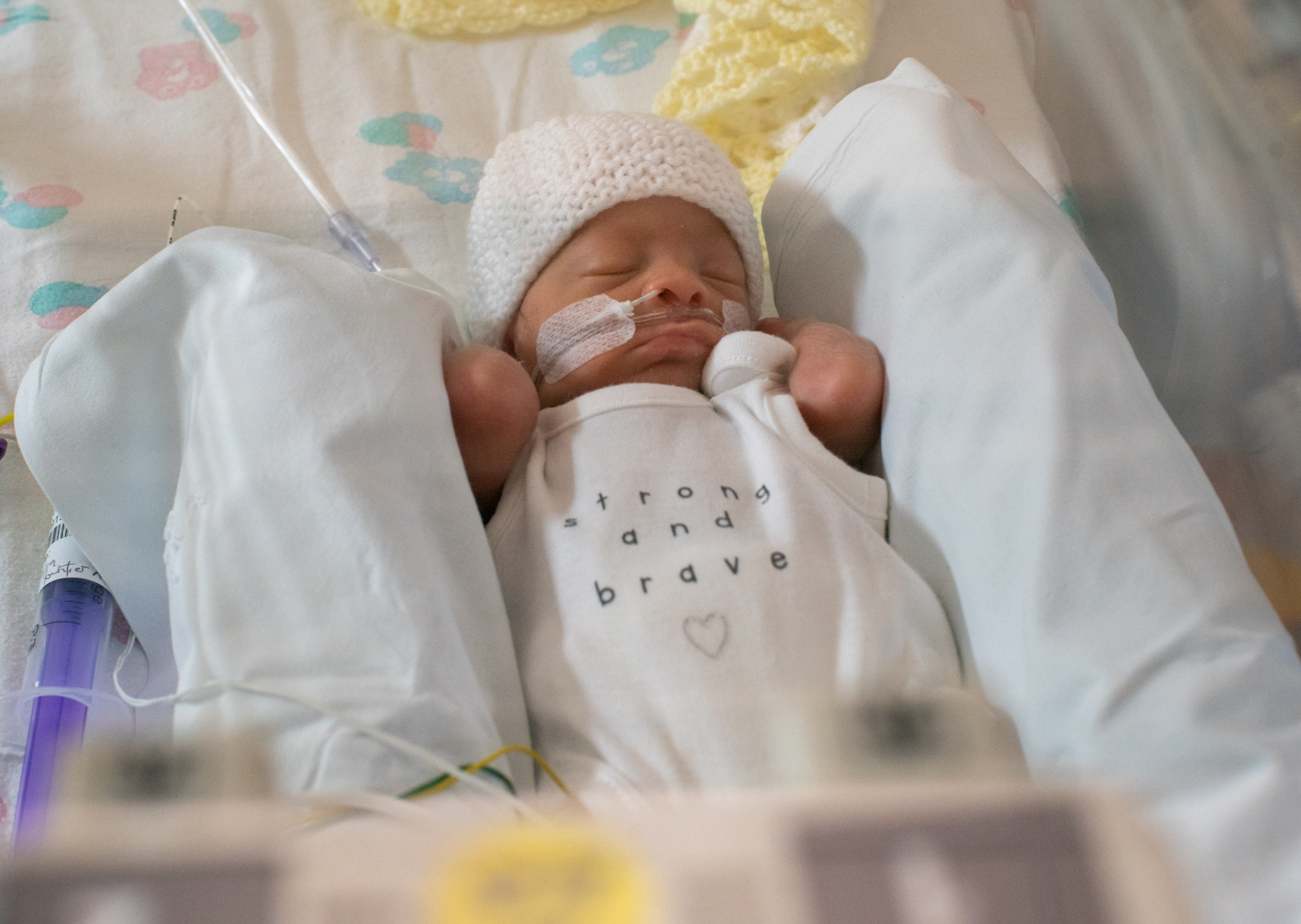 Baby Jaxon lies in his incubator in a white vest which reads Strong and Brave